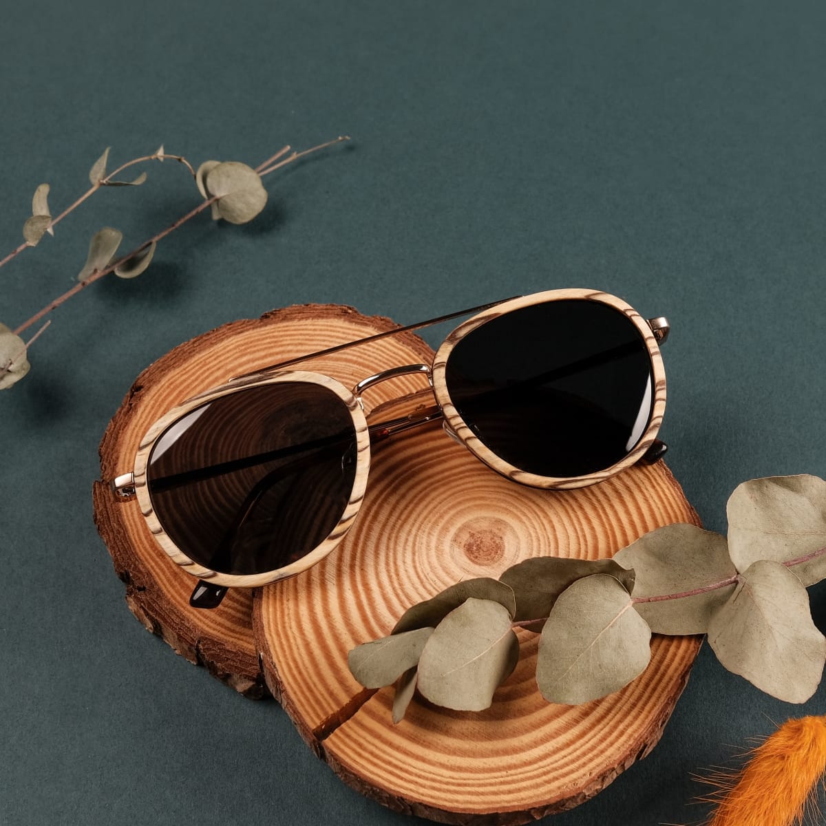 "The Risky" solbriller med zebrawood ramme og mat guld accenter på en rustik baggrund.