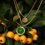 "Zendala Necklace" necklace featuring green nacre and gold, displayed on vibrant yellow berries for an elegant, natural look.