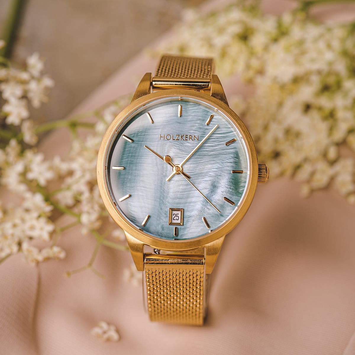 "Talamanca", elegante reloj con un dial de nácar y acentos de oro, enmarcado en un fondo floral.