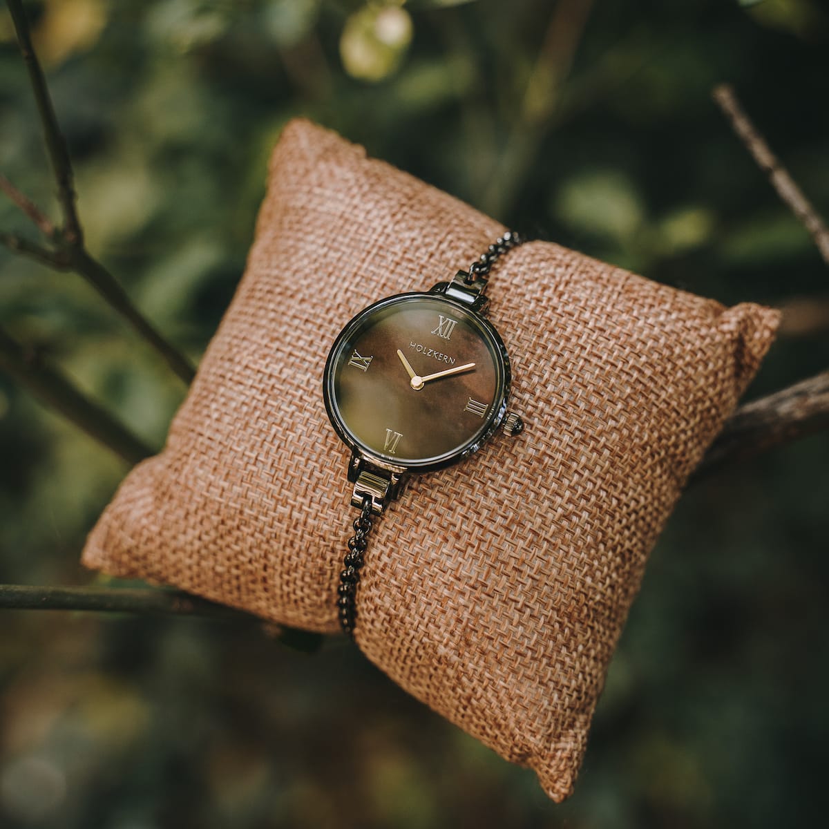 "Élisa" watch featuring a nacre dial and dark grey accents on a rustic burlap pillow.