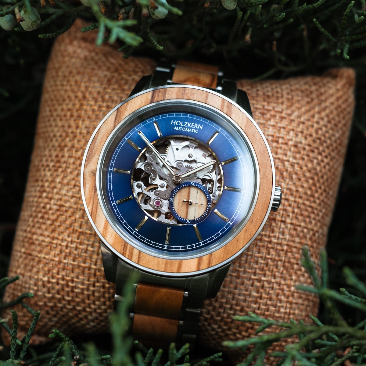 "Haiku" horloge met automatische beweging, met een olijfkleurig design en ingewikkelde details, tegen een geweven kussen.