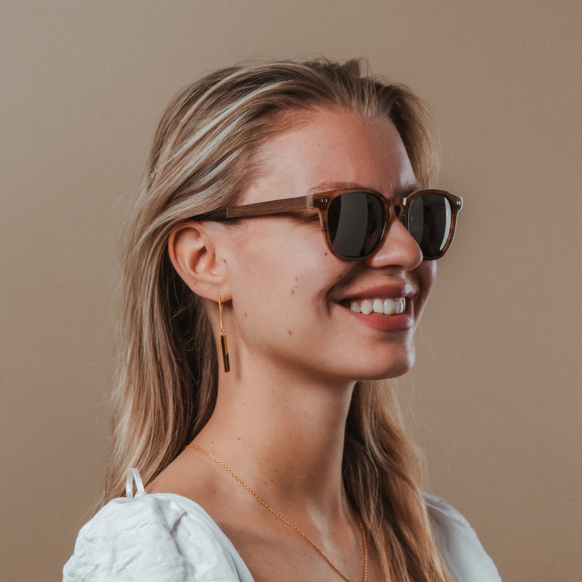 Les lunettes de soleil "The Comedian", au fini noyer et miel élégant, sont portées par une personne souriante.
