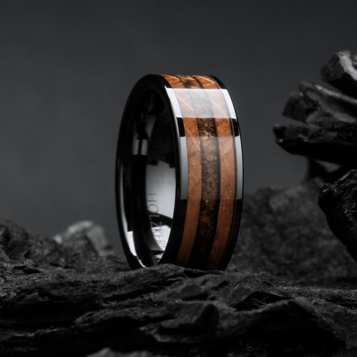 "Sumo Ring" : bague élégante en bois de whisky et céramique, placée sur un fond sombre et texturé.
