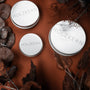 Wood Care Balm 100ml in sleek metal tins, styled with earthy tones and dried leaves.