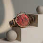 "Cheery", un reloj elegante con un dial rojo nácar y acentos cerámicos, elegantemente mostrado en una superficie geométrica.