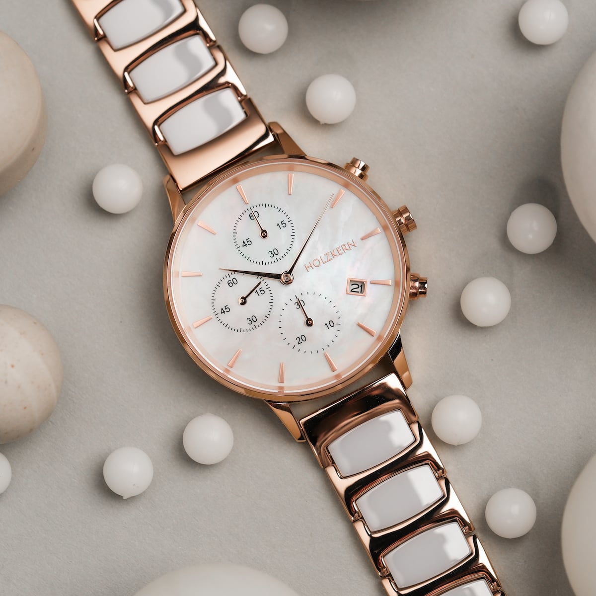 Reloj "Shiny" con esfera de nácar y enlaces cerámicos en un acabado de oro rosa, rodeado de esferas blancas.