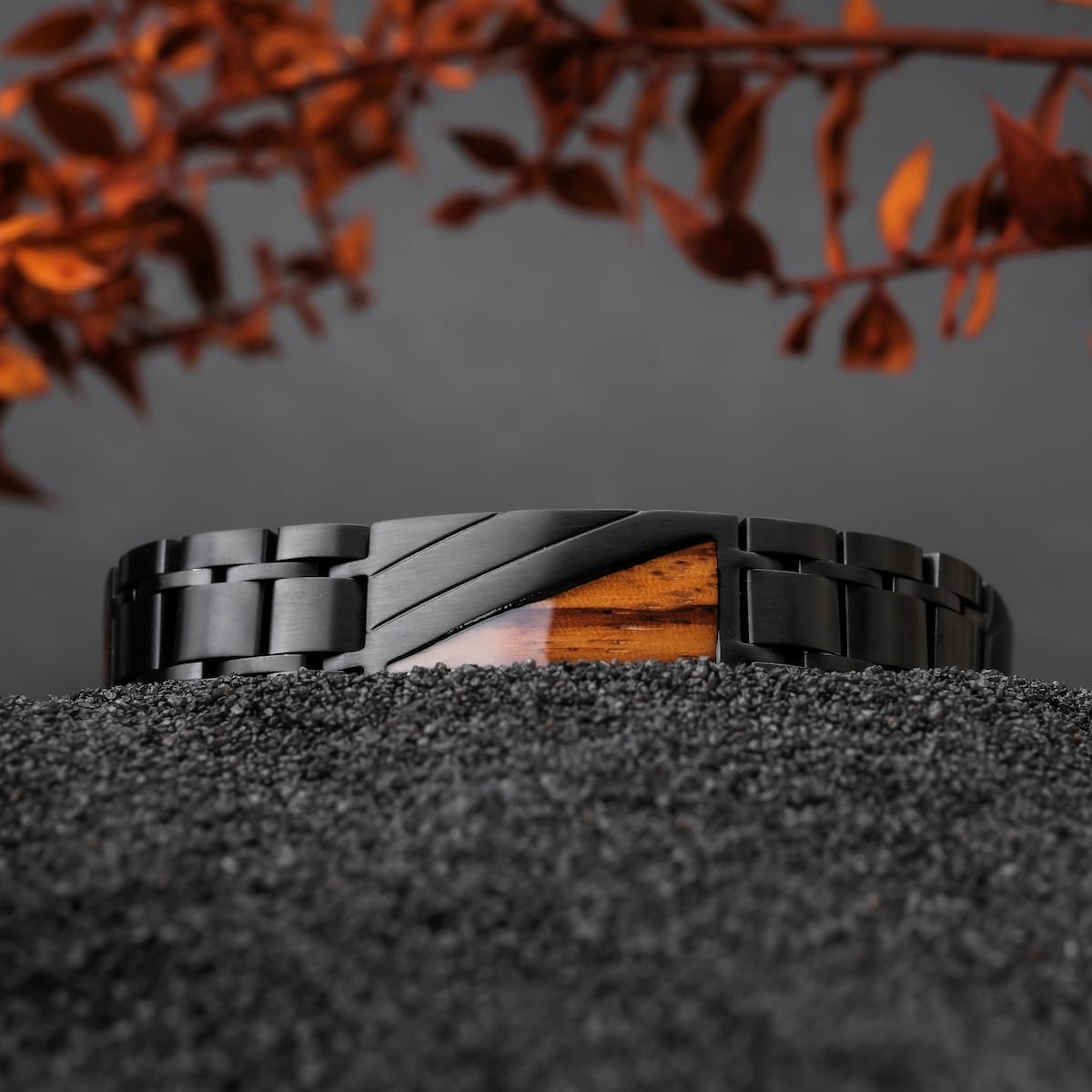 "Looper", et stilfuldt armbånd lavet af zebrawood og sort metal, hviler på en tekstureret sort overflade med efterårsblade.