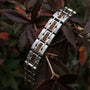"Tremolo", a stylish bracelet featuring a blend of walnut wood and silver elements, resting among deep-hued leaves.