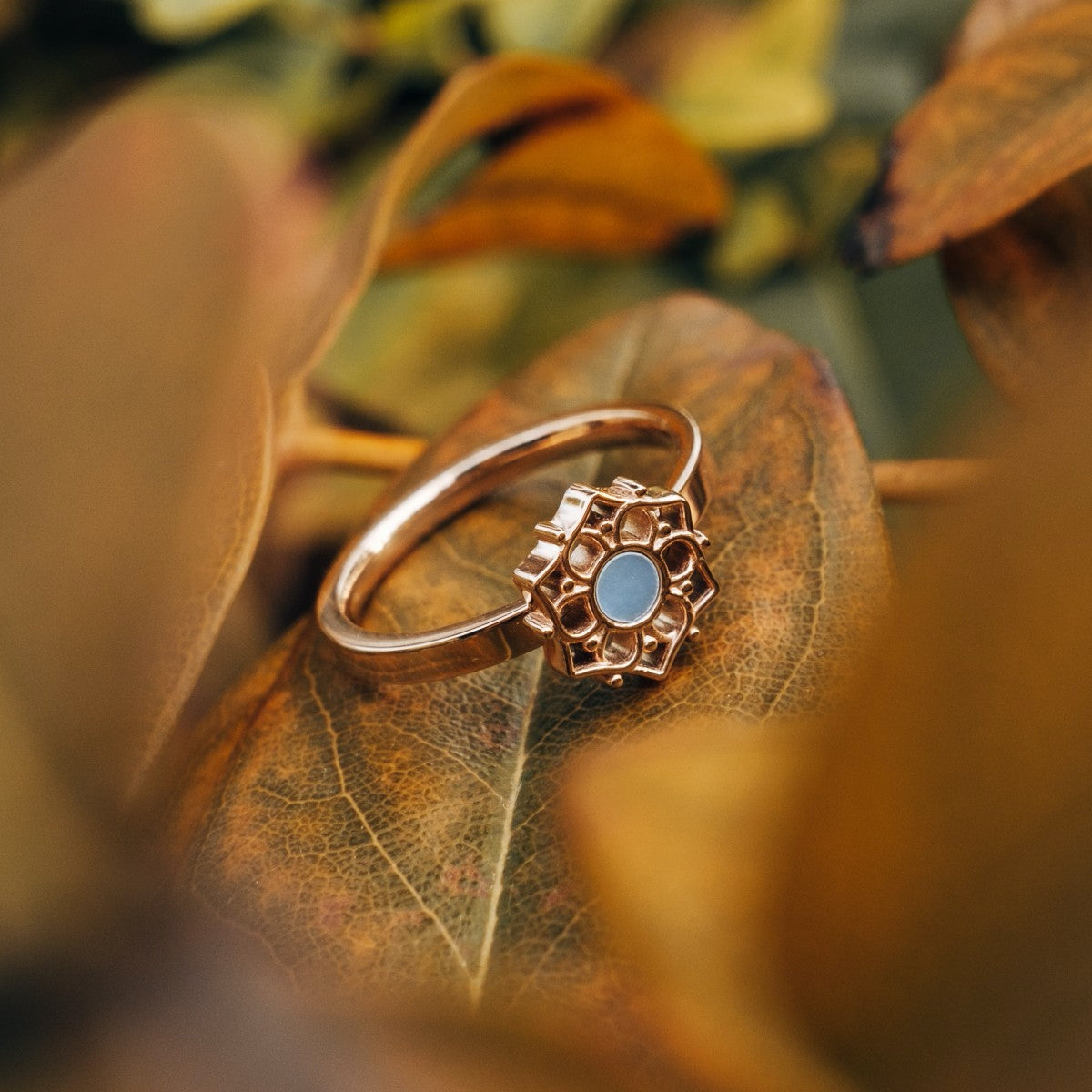 "Composition Ring", a rose gold ring featuring blue nacre, with an elegant floral design set against autumn leaves.