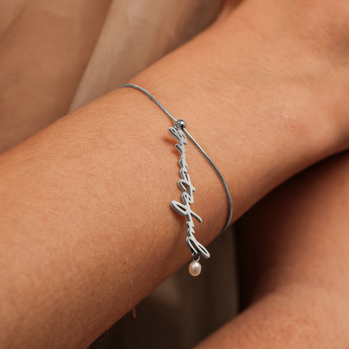 "Gratinal-Charm" armbånd med elegante perler og en sølv charme med en minimalistisk design på håndleddet.