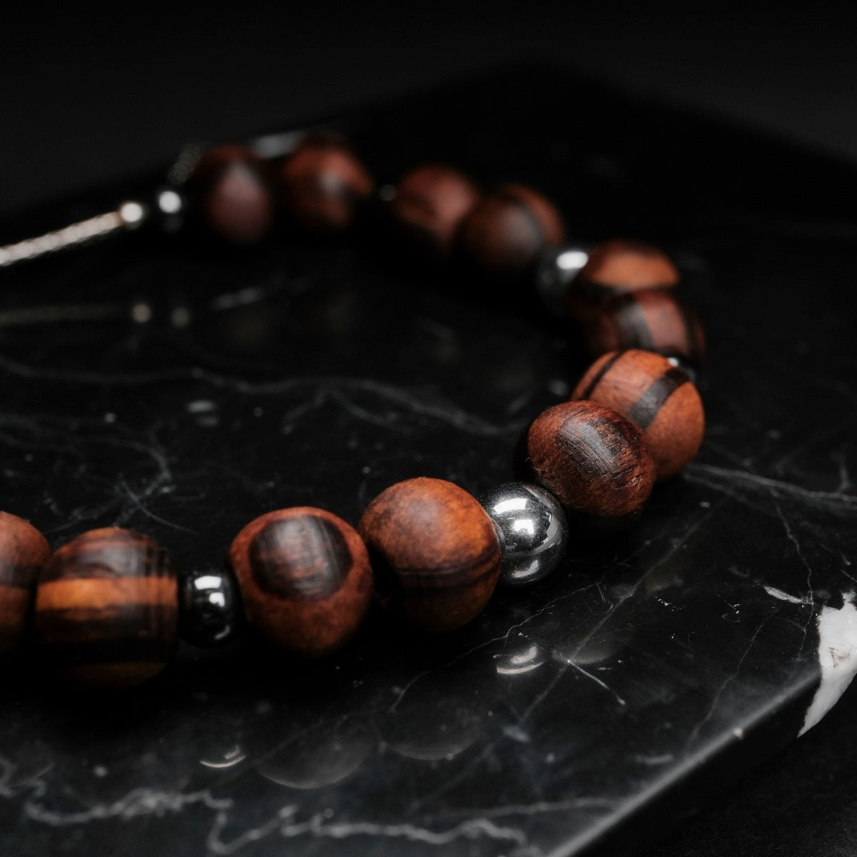"Superset", a stylish bracelet, features hematite and walnut beads on a dark marble background.