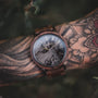 "Leonardo" watch featuring a walnut and marble design on a tattooed wrist, highlighting its rustic elegance.